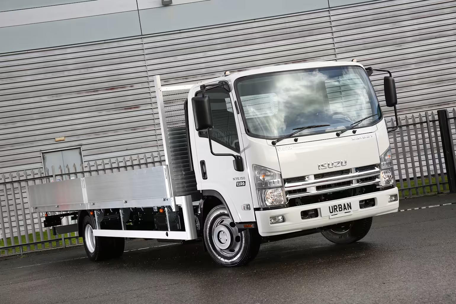 White Isuzu N55 150 chassis cab flatbed truck with aluminium side panels, viewed at an angle outside a workhouse.