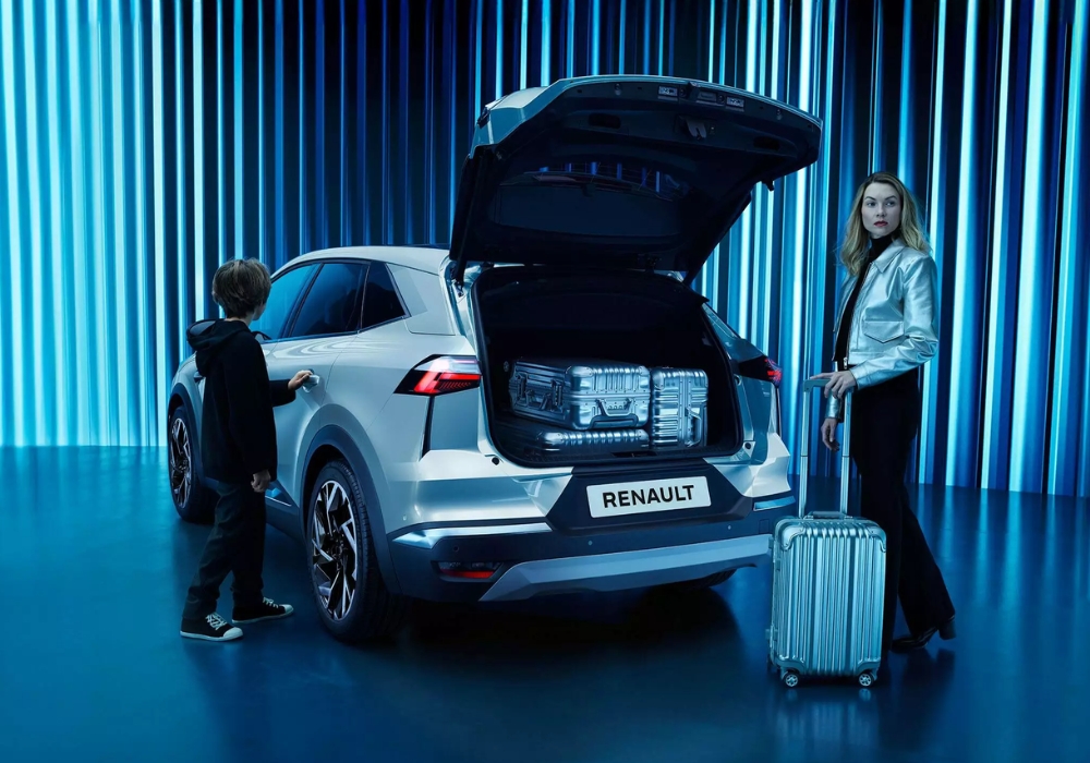 Rear three-quarter view of Renault Symbioz with boot open, showing illuminated cargo space, with a woman and child beside the vehicle.