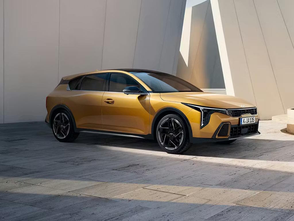 Front three-quarter view of the Kia K4 in striking gold metallic, featuring signature LED daytime running lights, sculpted body lines and bold multi-spoke alloy wheels.