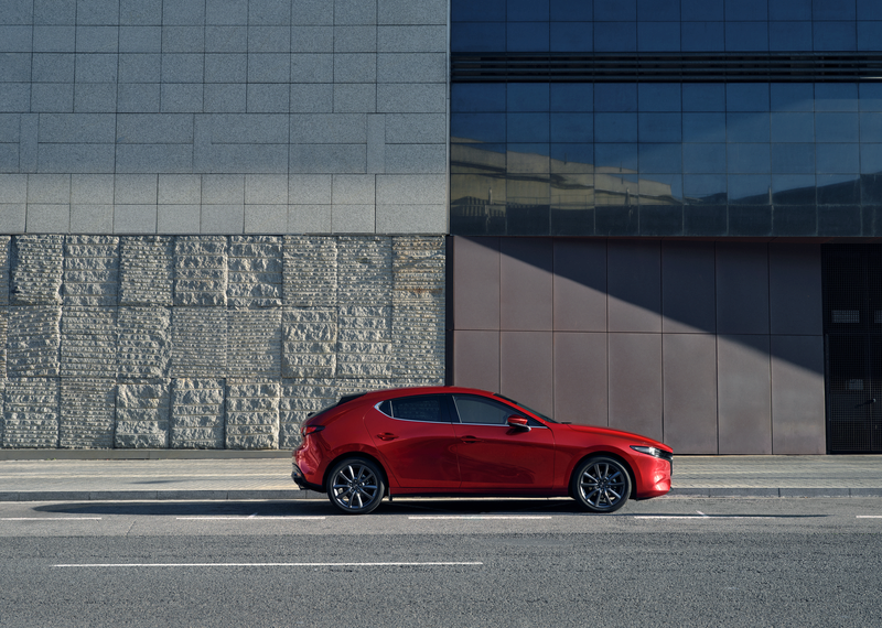 A side angle of a red Mazda 3 car parked on the side of a road.