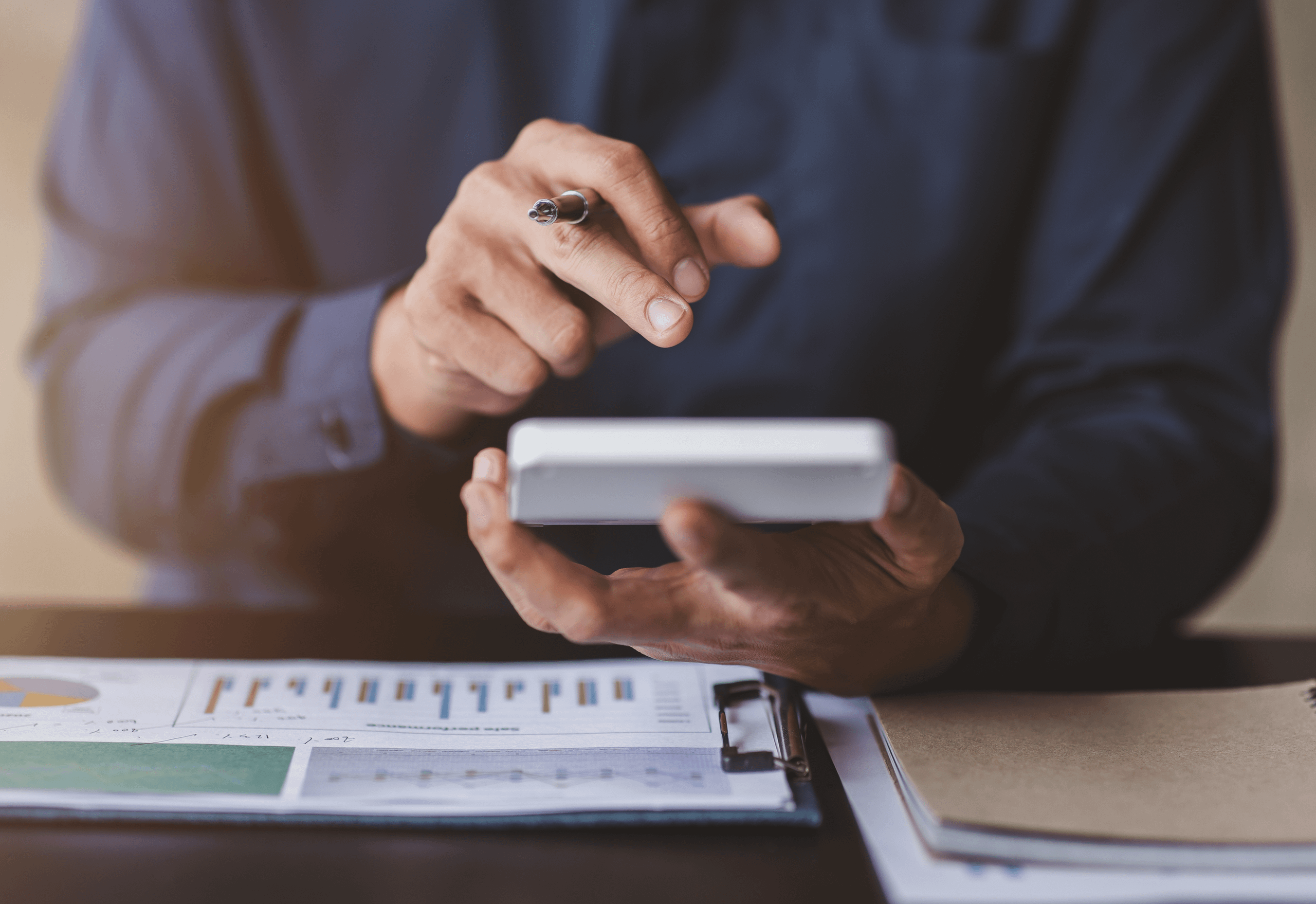 Man sat at desk with a calculator in hand and paperwork on the desk.