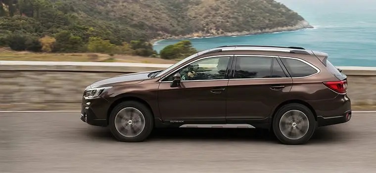 Brown Subaru Outback driving along road side view
