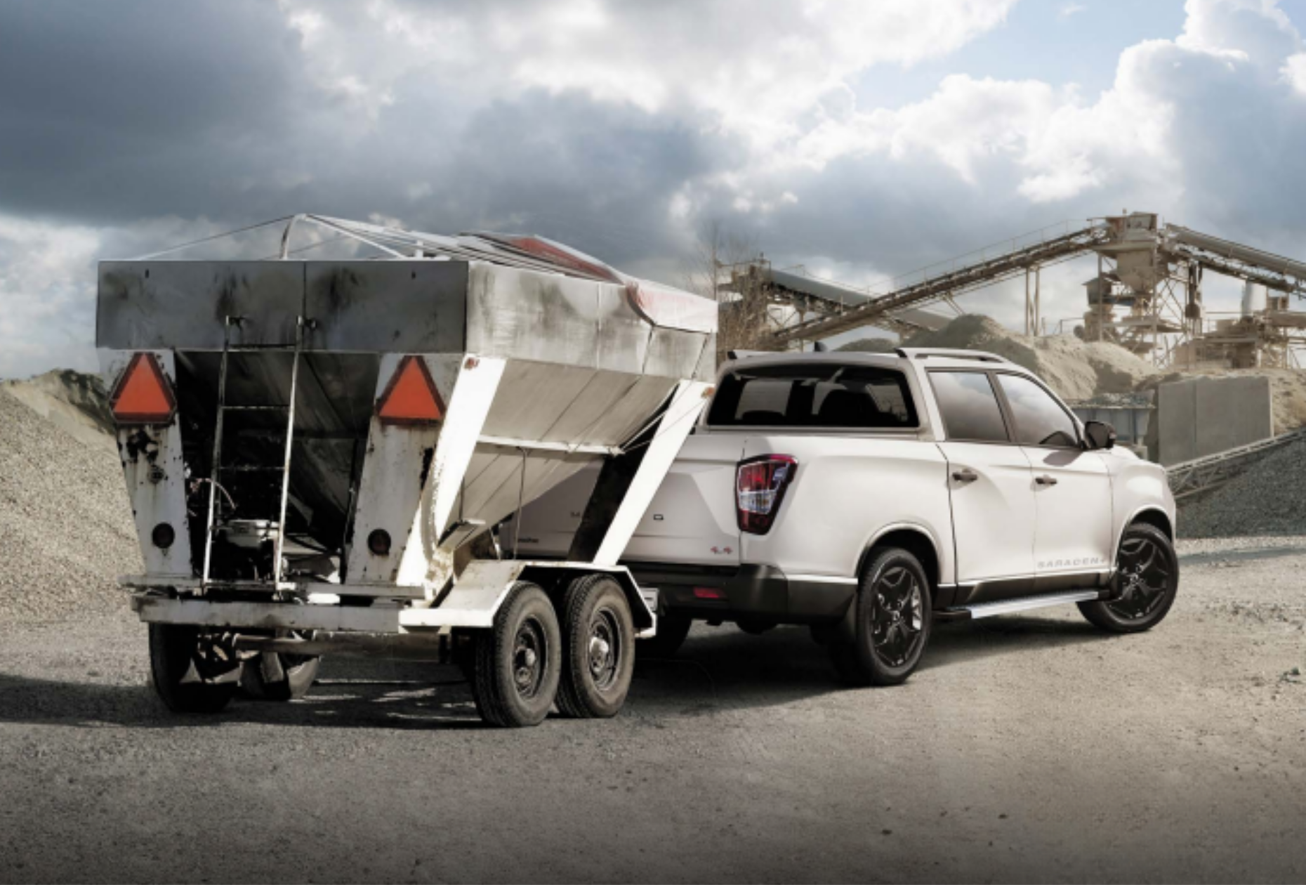 White KGM Musso pulling construciton equipment at worksite