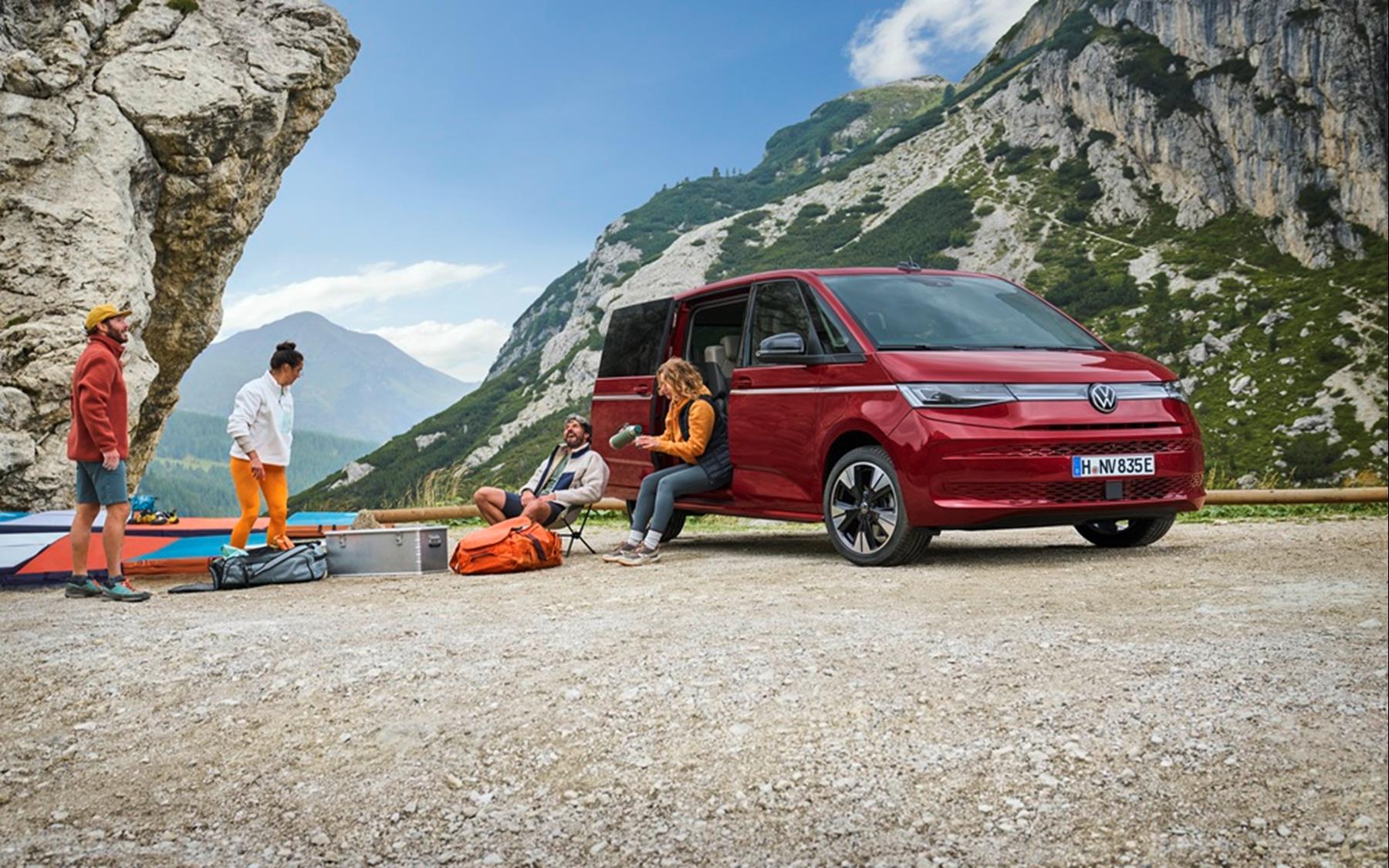 Red VW Multivan with sliding door open, parked in the mountains as friends unpack climbing gear beside it