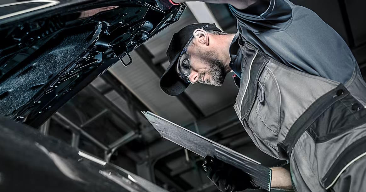 Mechanic inspecting a vehicle with a clipboard in a workshop.