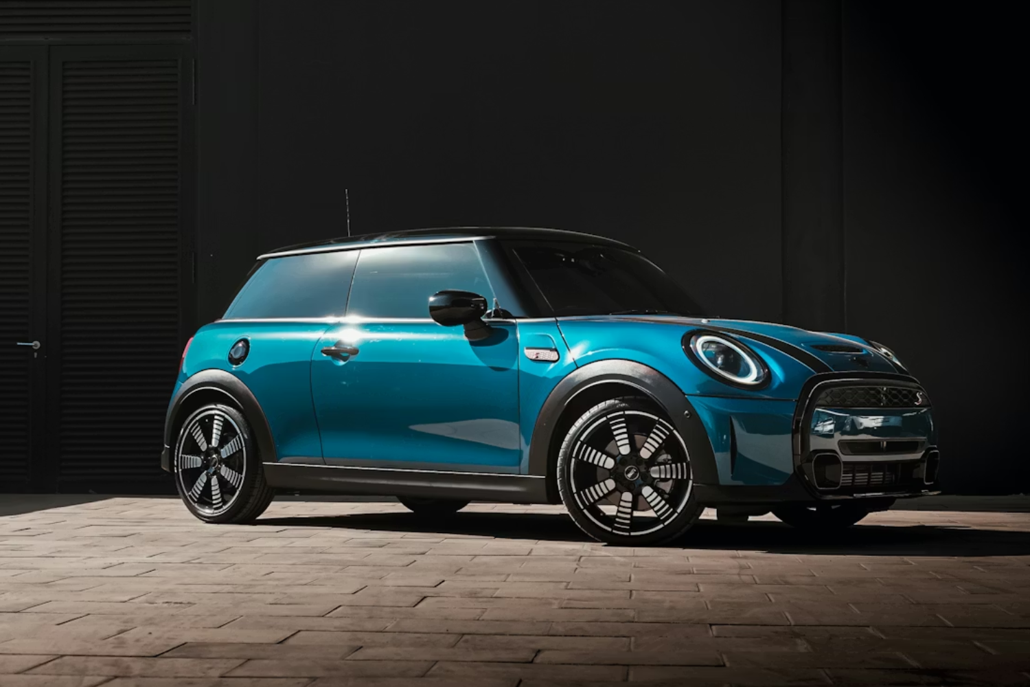 Teal Mini hatchback parked outside modern building.