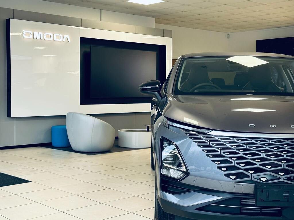 Front three-quarter view of a grey Omoda SUV in the Omoda Louth showroom, featuring distinctive geometric grille design and sharp LED headlight signatures