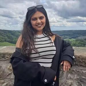 Person standing at a scenic viewpoint overlooking rolling countryside beneath a cloudy sky.