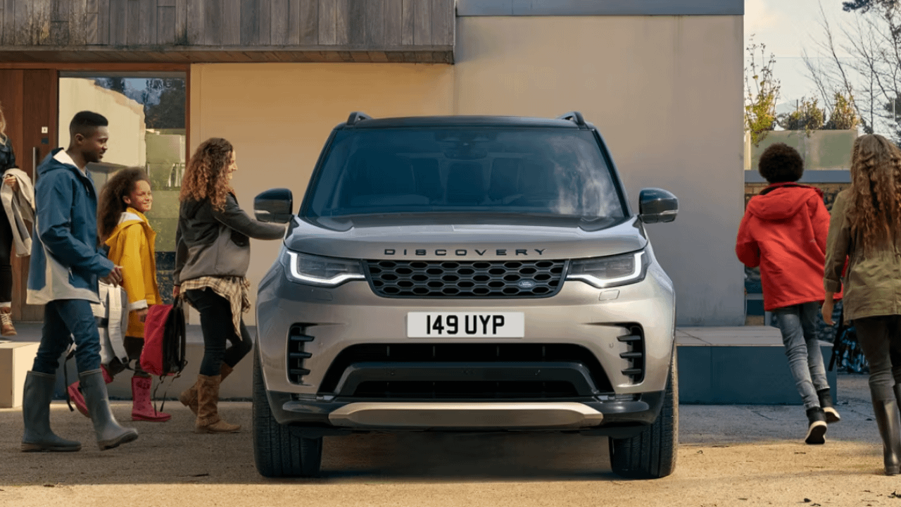 Front view of a Land Rover Discovery parked outside a home while a family with children walks around it.