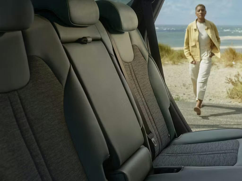 Interior view of the Kia Sorento rear cabin, featuring premium olive-green leather seats with woven fabric centre inserts and integrated headrests, viewed through an open door at a coastal location.