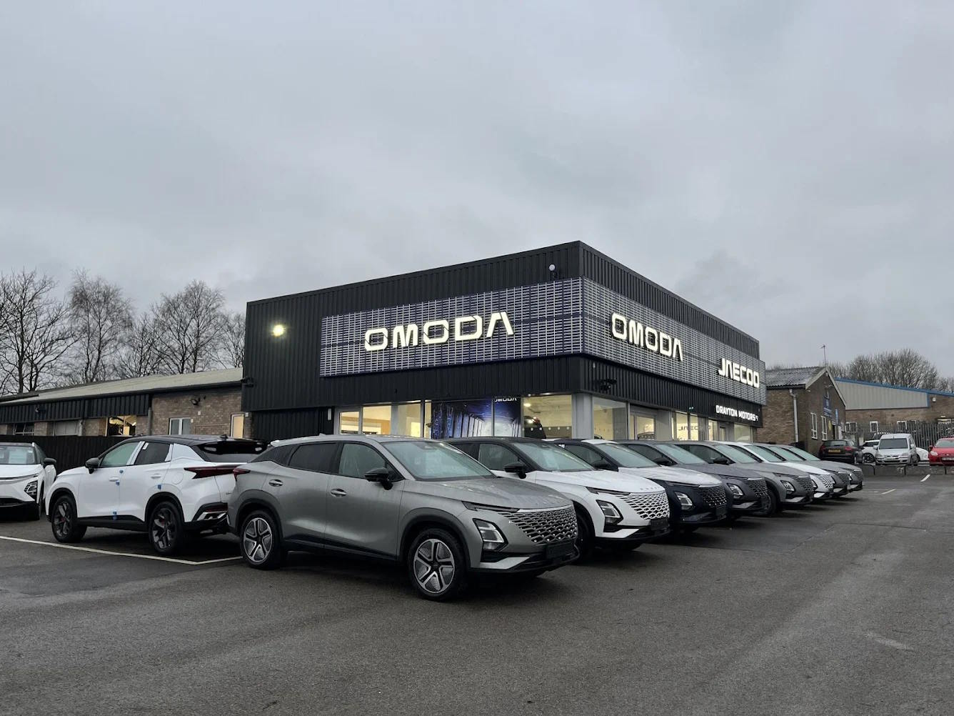 Row of Omoda SUVs displayed in white, silver and grey outside the Omoda and Jaecoo dealership in Grantham, featuring modern dark-clad showroom architecture.