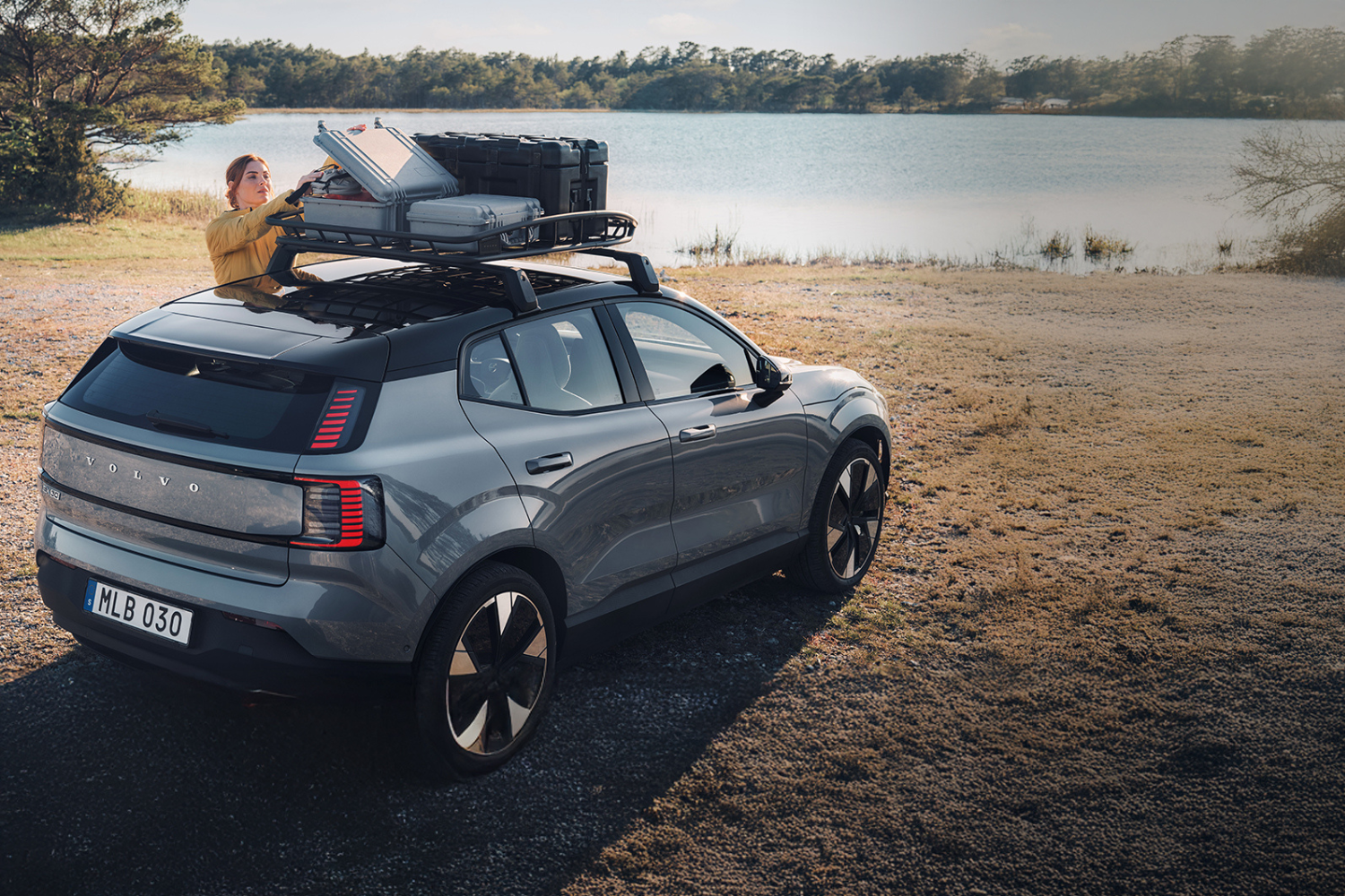 Grey Volvo SUV with roof rack and luggage beside lakeside.