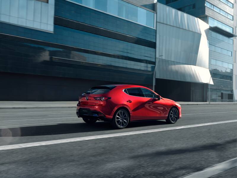 A red Mazda3 hatchback driving along a road.