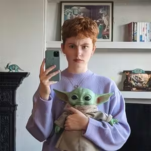 Indoor portrait of a person holding a character toy while taking a mirror photograph.