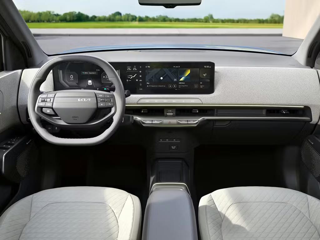 Interior view of the Kia EV2, featuring a modern dual-screen digital display, two-spoke steering wheel with integrated controls and light grey quilted seats.