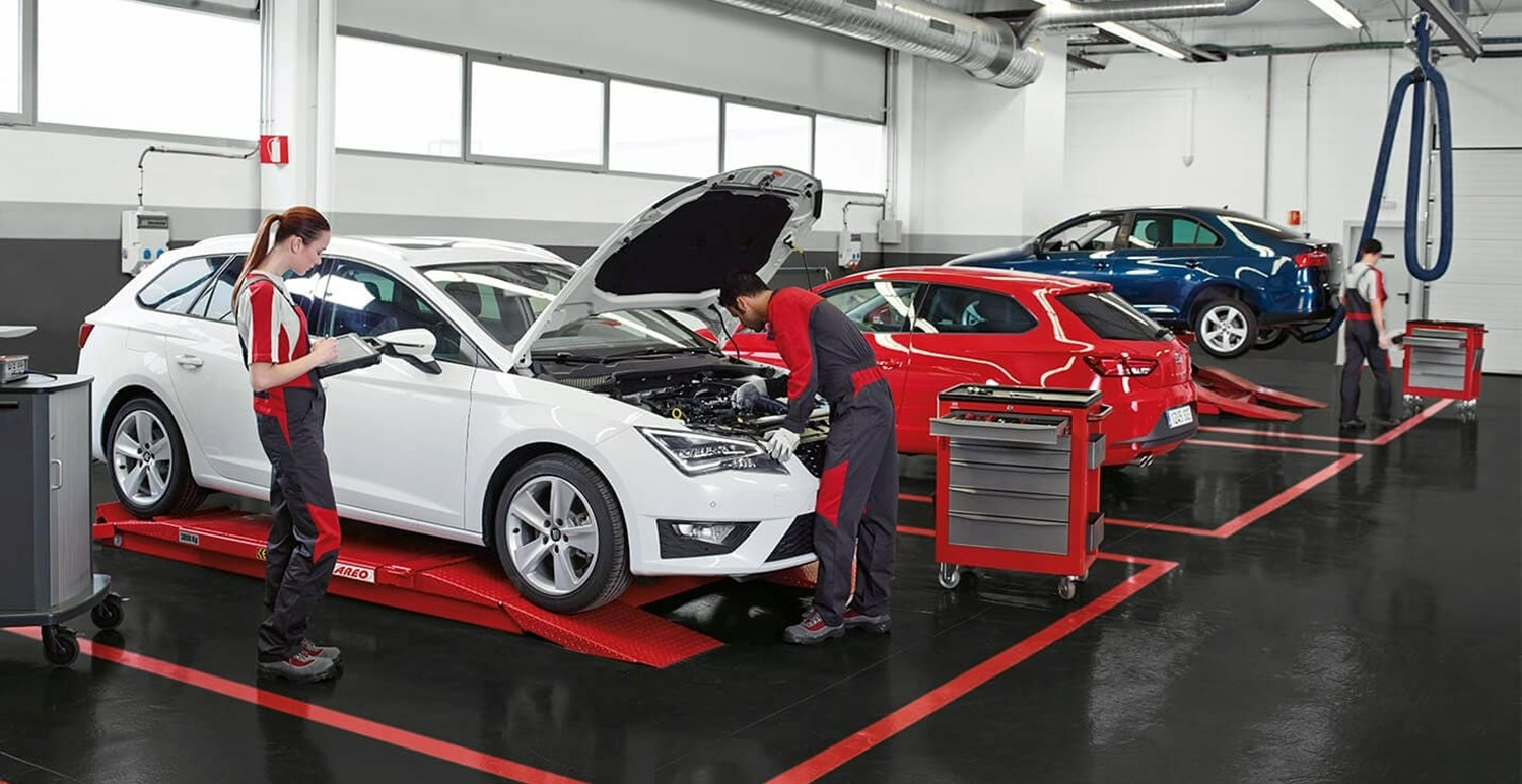 Technicians inspecting SEAT vehicles in a clean workshop, with a white SEAT on a lift being serviced and additional SEAT models positioned on ramps in the background.