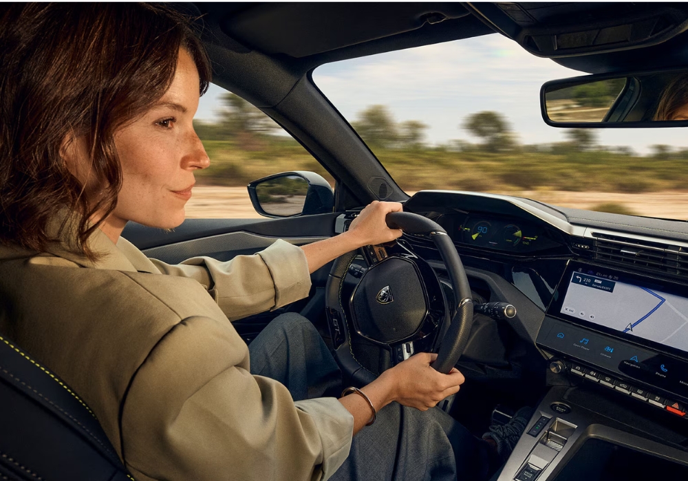 Interior of Peugeot 308 SW showing a woman driving with hands on the steering wheel and infotainment screen visible.