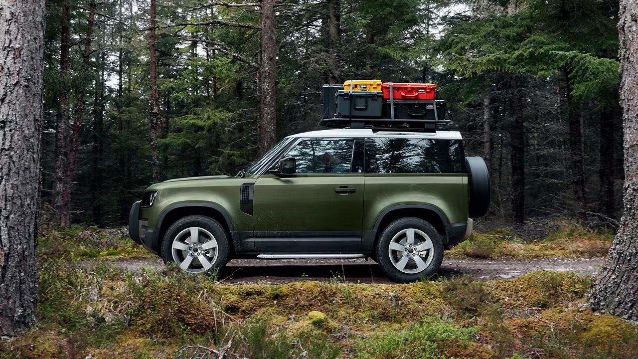 Green Defender 90 parked on a forest track with roof cargo boxes.