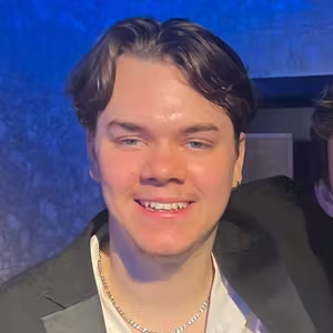 Close-up portrait of a person wearing a blazer and necklace at a venue.