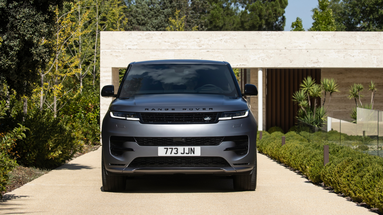 Front view of a grey Range Rover parked in the driveway of a modern home surrounded by landscaped greenery.