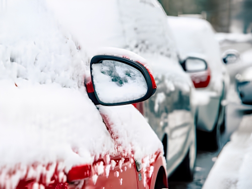 Vehicle covered in snow with icy side mirror during winter conditions.