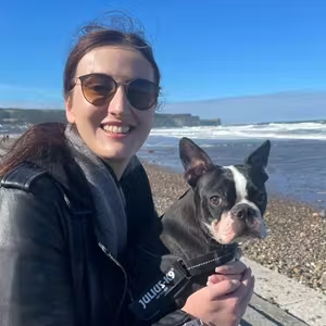 Person and Boston Terrier enjoying a coastal walk beside the shoreline on a clear day.