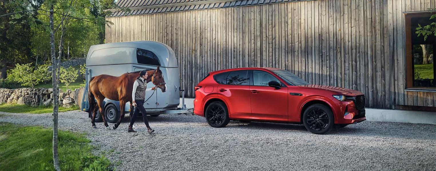 Red Mazda CX-60 with a horse trailer parked outside a modern shed.