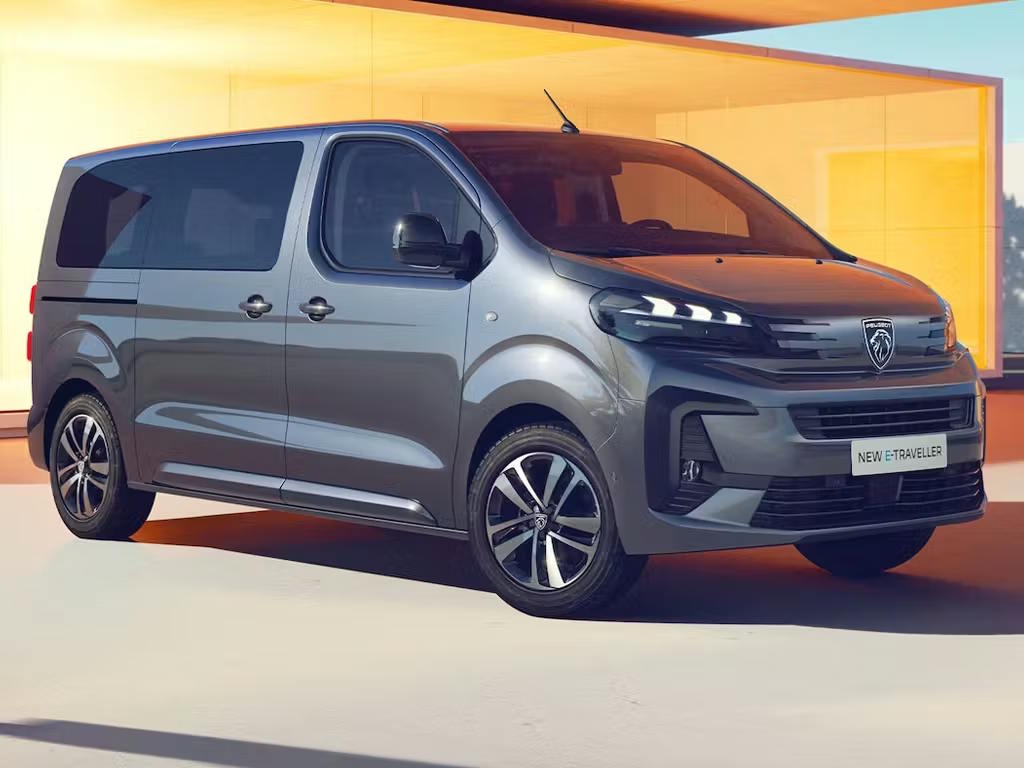Front three-quarter view of the new Peugeot E-Traveller in grey, featuring distinctive LED daytime running lights, bold lion badge and spacious MPV silhouette with sliding rear doors.