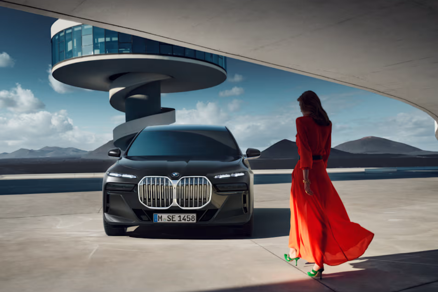 Woman in red dress walking towards black BMW sedan.