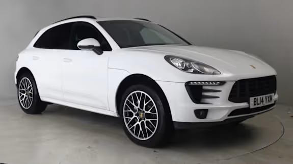 White Porsche Macan SUV parked in a studio against a light grey background, viewed from the front three‑quarter angle.