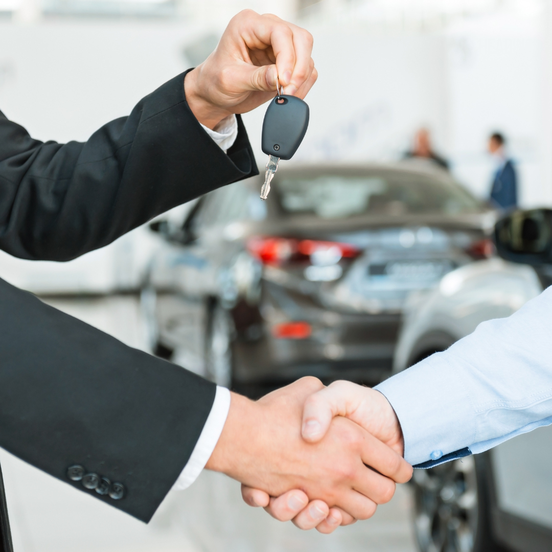 arms handing over keys to another person - one hand shaking the other and one hand holding car keys