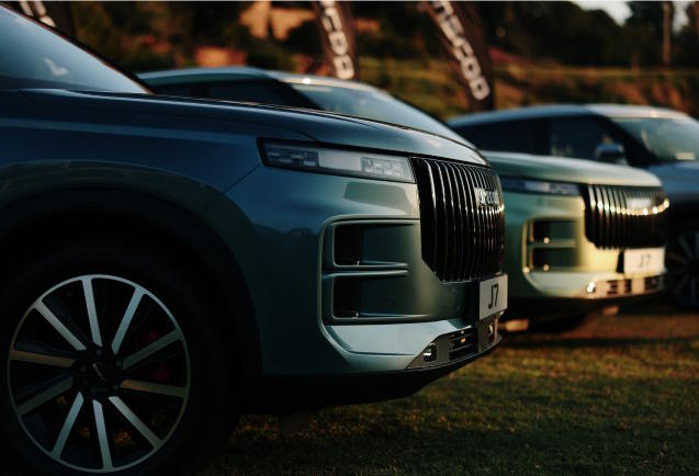 Front three-quarter view of the Jaecoo J7 SHS Hybrid SUV in teal, featuring the bold vertical grille design, distinctive LED headlight signature and striking two-tone alloy wheels.