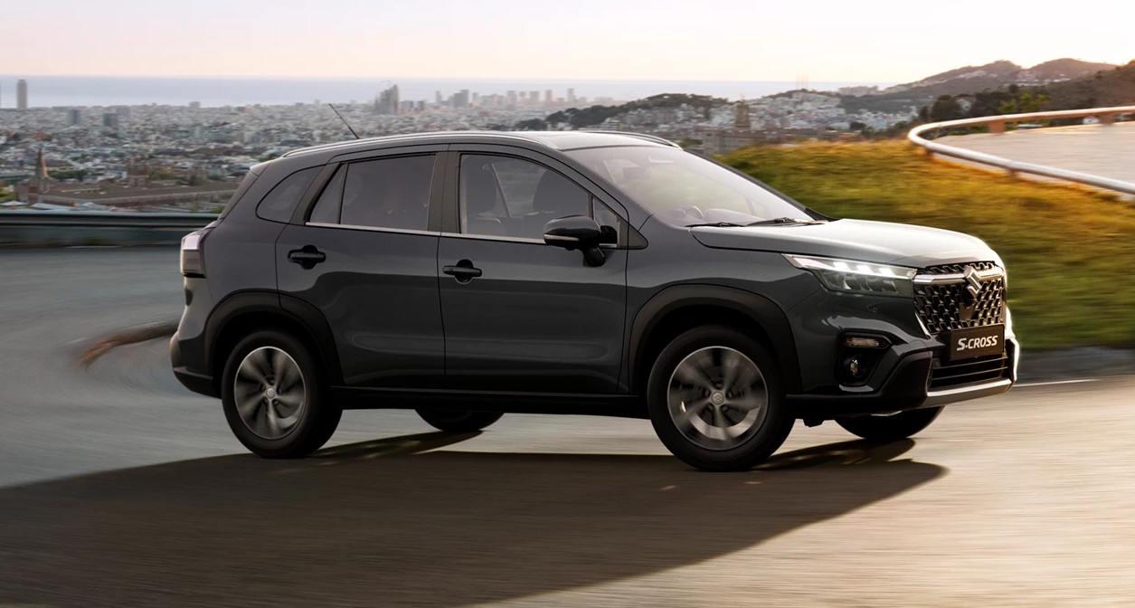 Dark grey Suzuki S‑Cross SUV driving on a curved road above a city, shown in side profile.