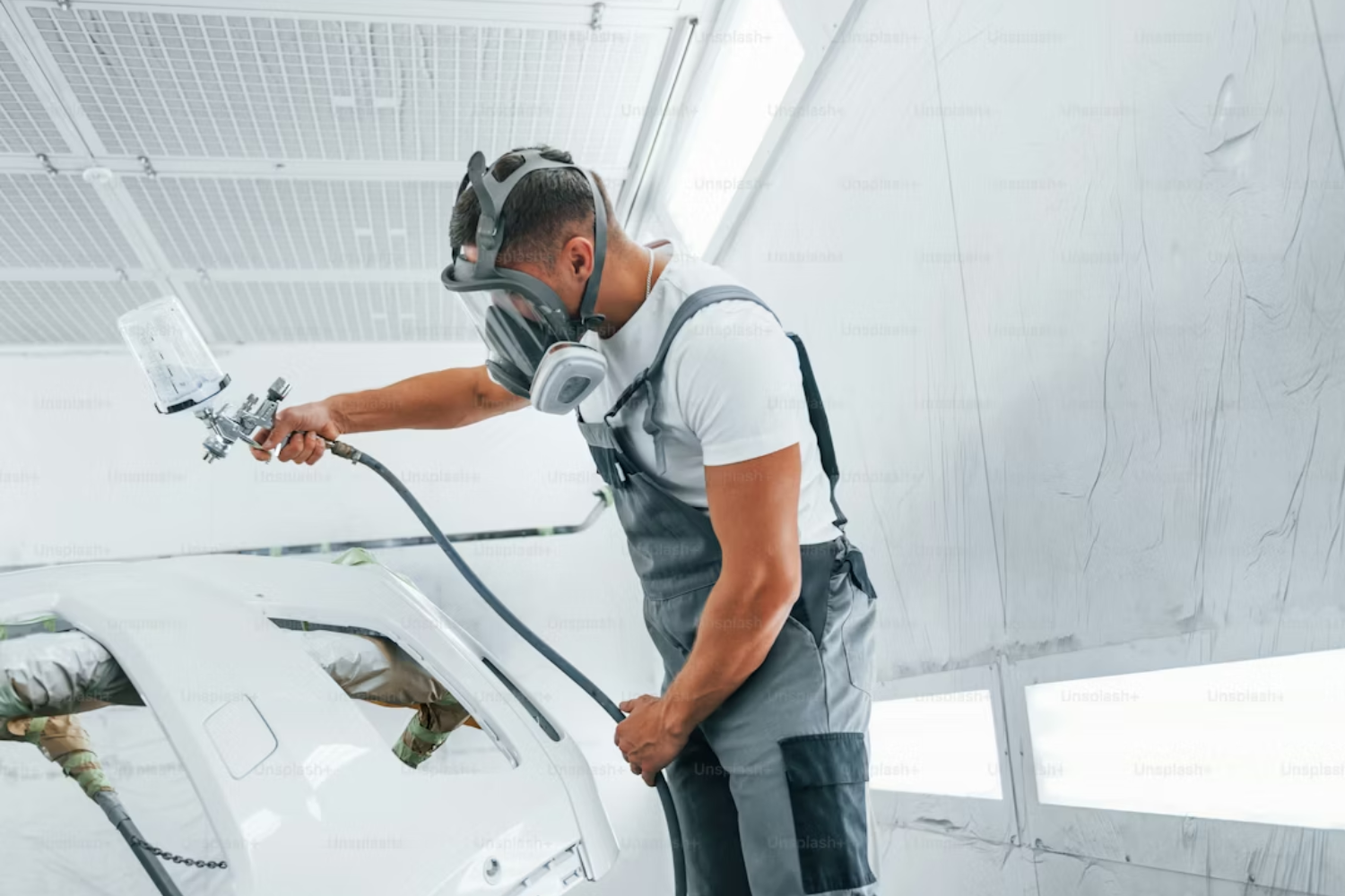 Technician spray painting car panel in bodyshop.