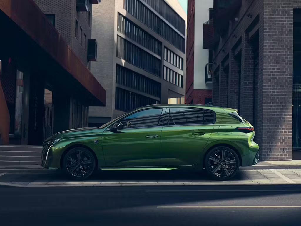 Peugeot 308 hatchback parked in an urban setting, showcasing its aerodynamic profile, sculpted bodywork and stylish alloy wheels.