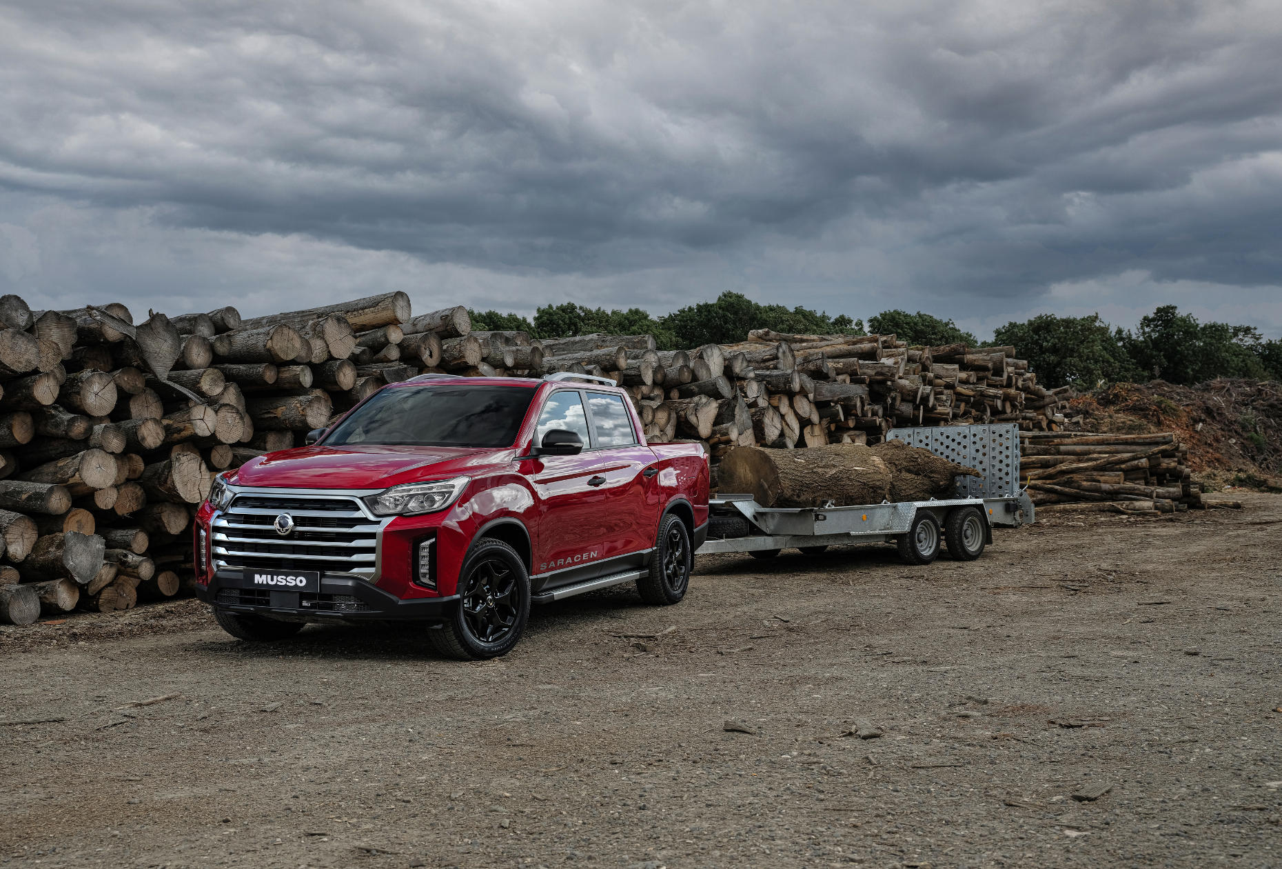 RED KGM MUSSO pulling logs on a trailer