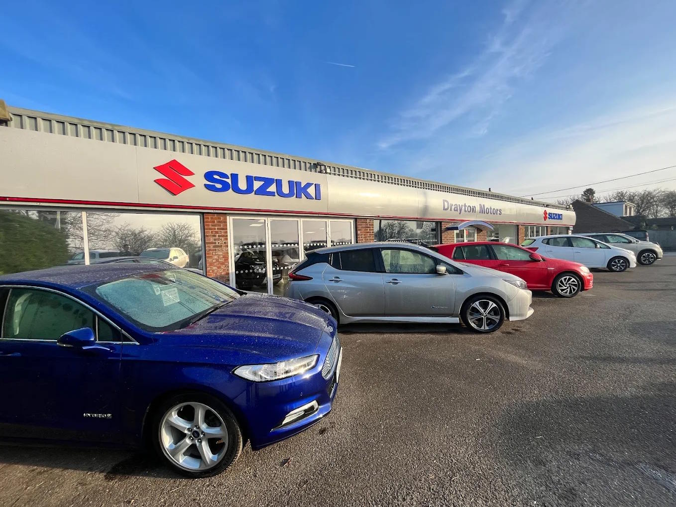 Drayton Motors Suzuki Boston dealership exterior with a selection of quality used cars on the forecourt, including a blue Ford Mondeo and silver Nissan Leaf.