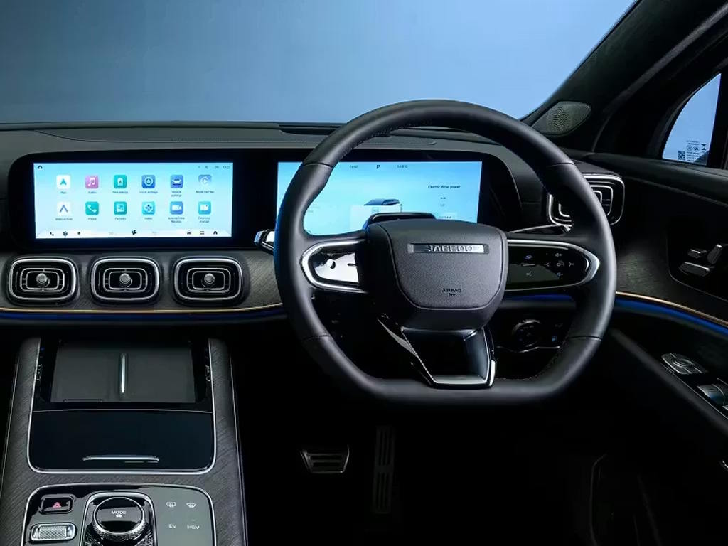 Interior view of the Jaecoo 8 SUV, featuring a dual-screen dashboard layout, leather-wrapped steering wheel, distinctive oval climate vents and ambient blue lighting accents.