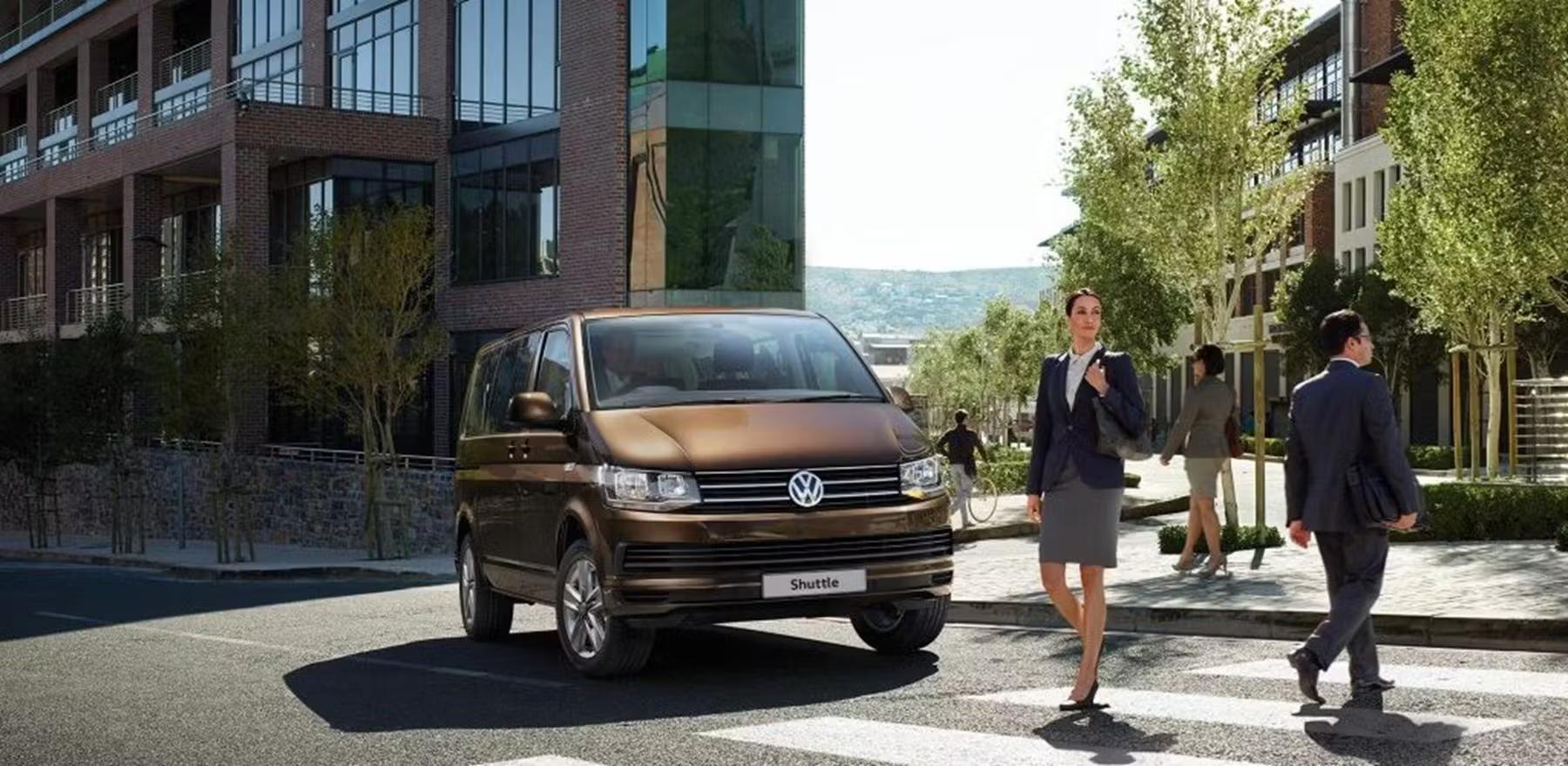 Person crossing the road in front of a Brown Volkswagen Transporter Shuttle