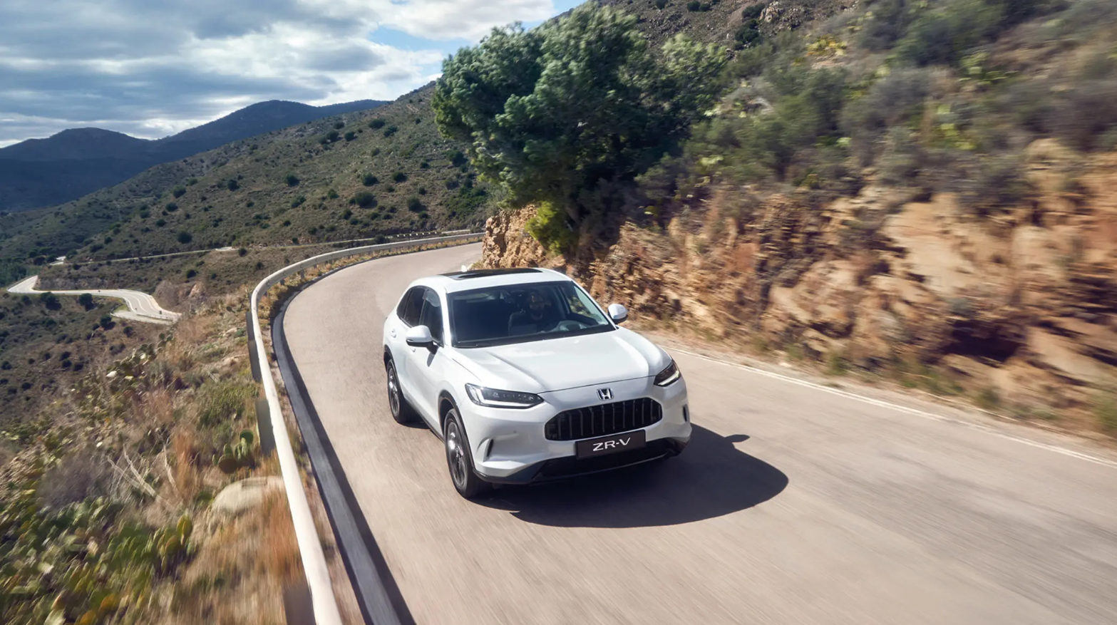 White Honda ZR-V Hybrid driving through mountainous landscapes.