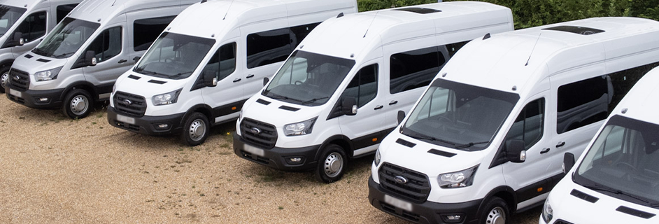 Row of white minibuses parked in a lot, viewed from above.