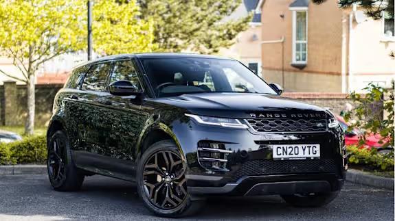 Black Range Rover Evoque SUV parked on tarmac in front of houses and trees, viewed from the front three‑quarter angle.