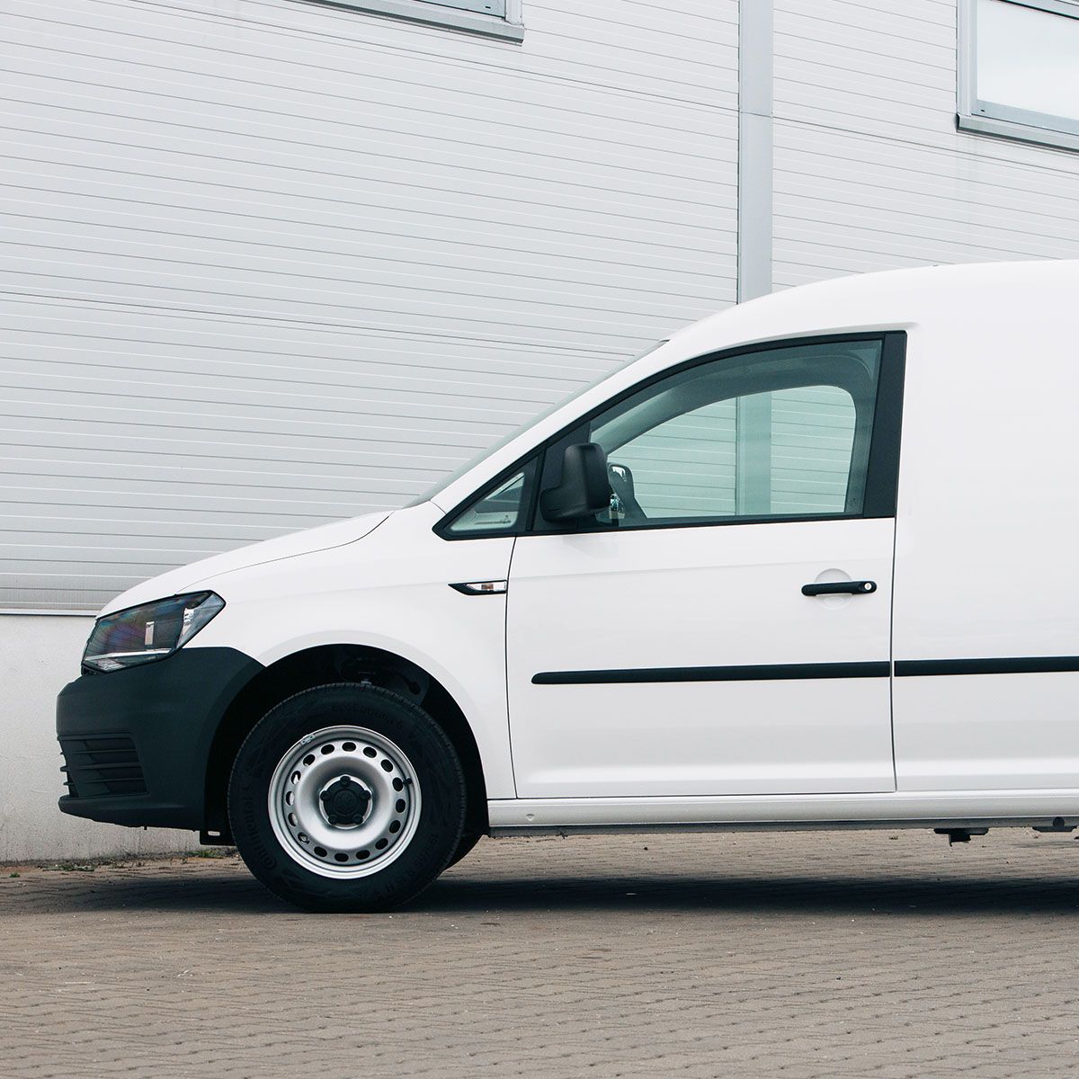 Side view of a white commercial van parked outside an industrial building.