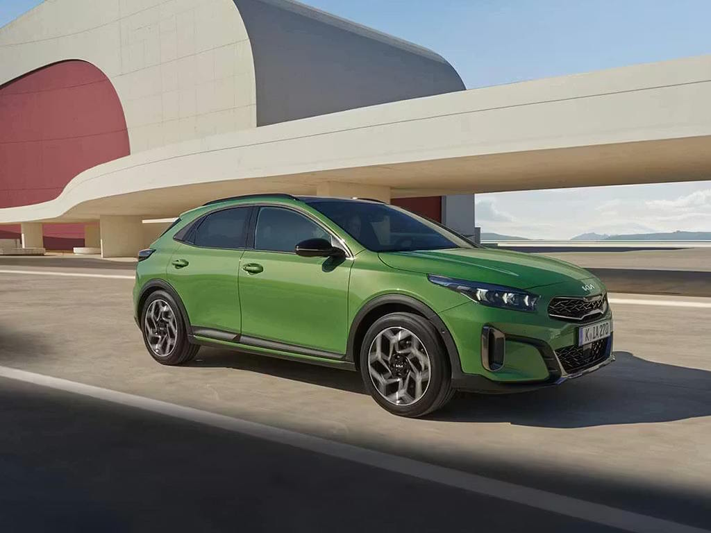 Front three-quarter view of the Kia XCeed crossover in vibrant green, featuring the signature tiger-nose grille, sharp LED headlights and sculpted alloy wheels against modern architecture.