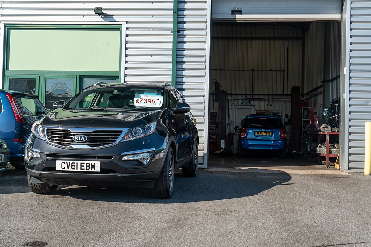 Kia for sale, parked outside of dealership car in workshop on the right 