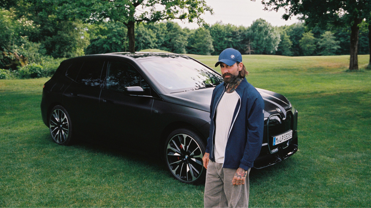 Man standing beside black BMW SUV on grass.