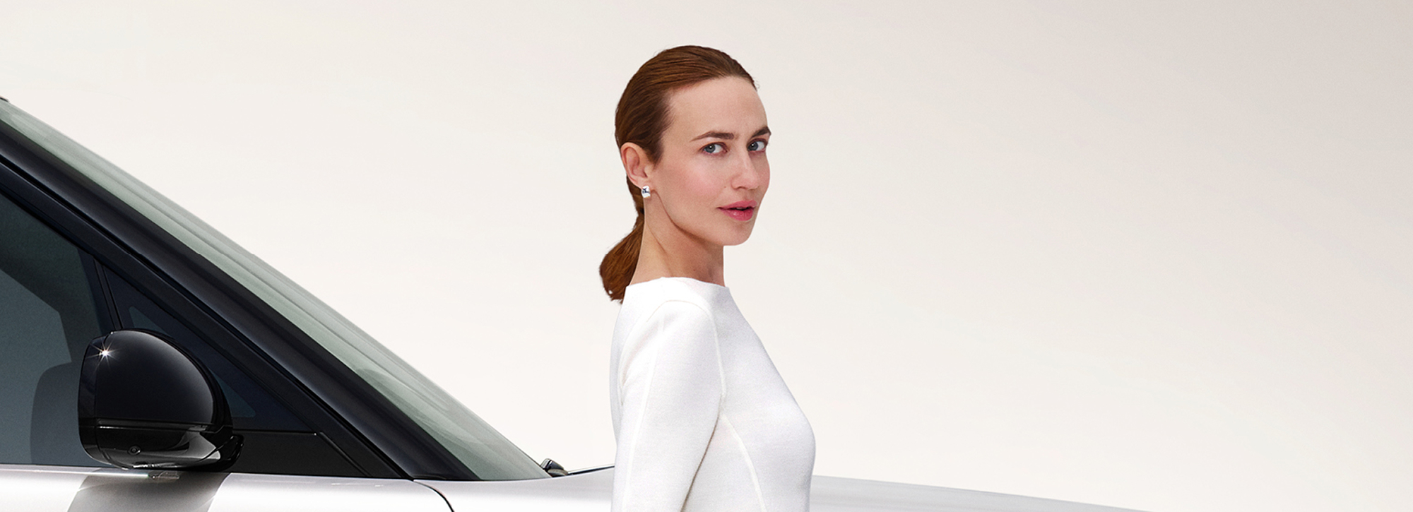 Closeup of a woman standing beside white Range Rover in studio setting.