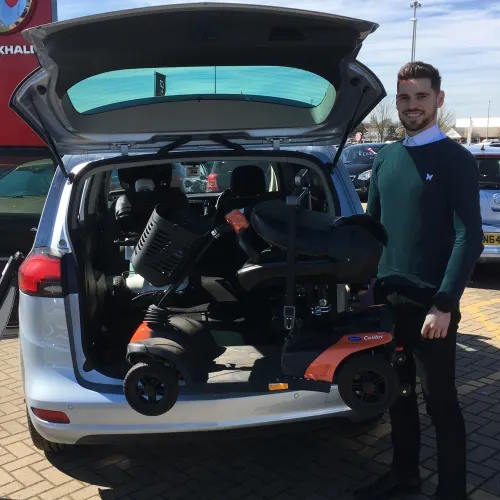 Motability Scooter folded away in the back of a car with man stood on the right.