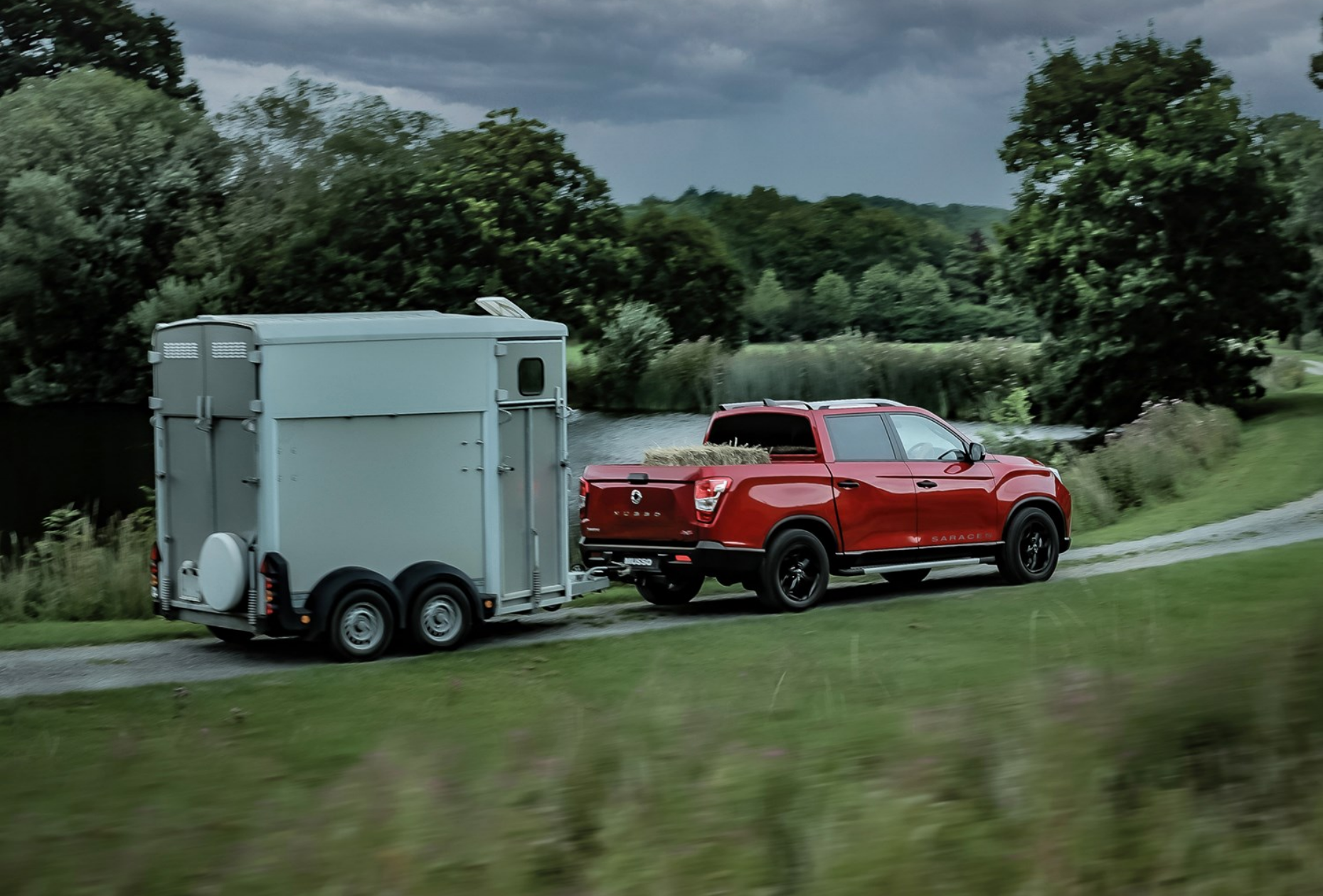 Red KGM Musso towing a horse box along a country road with trees and grass surrounding