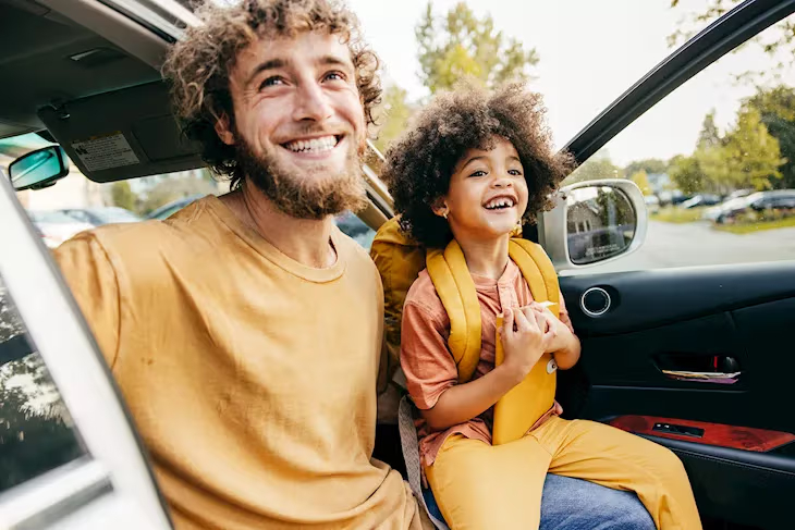 Adult and child smiling while seated inside a car, highlighting a comfortable and family-friendly motoring experience.